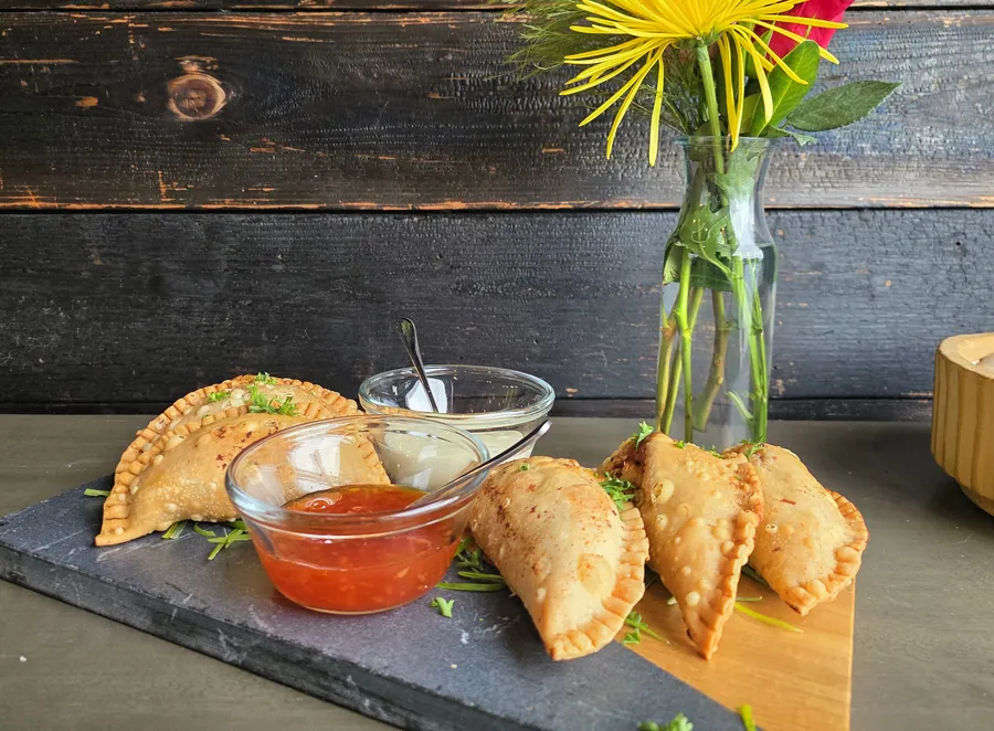 Empanadas and dipping sauces on a slate board next to a vase of flowers