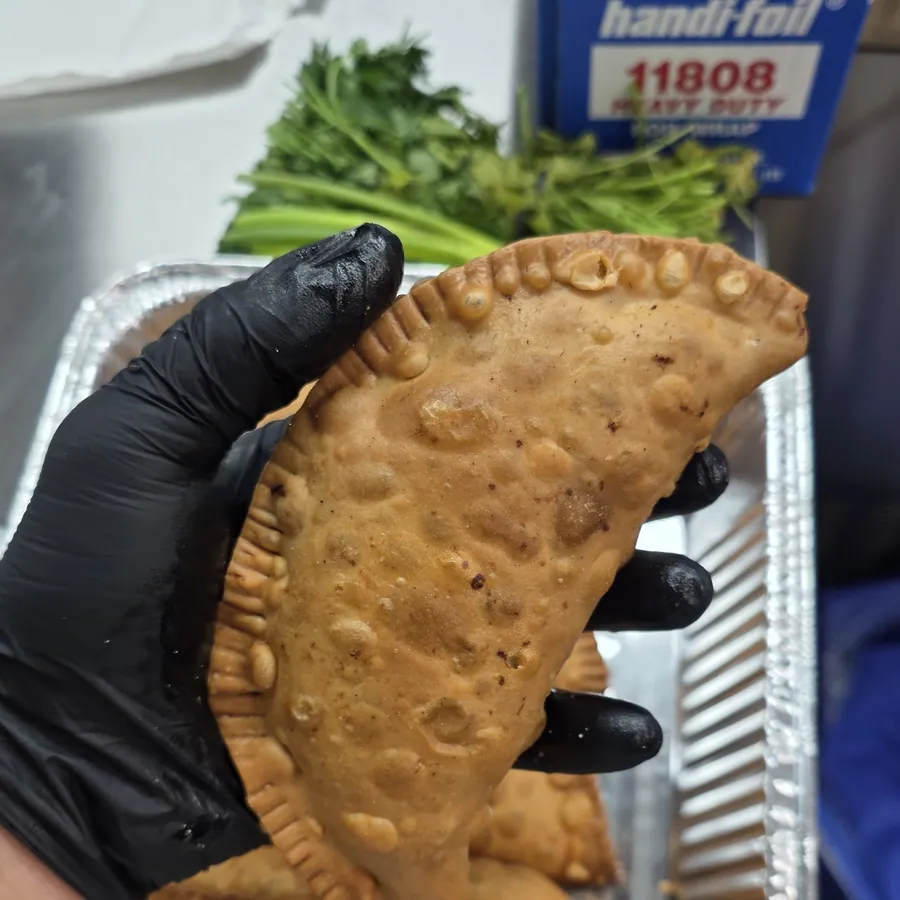 A gloved hand holding up a golden empanada fresh from the fryer