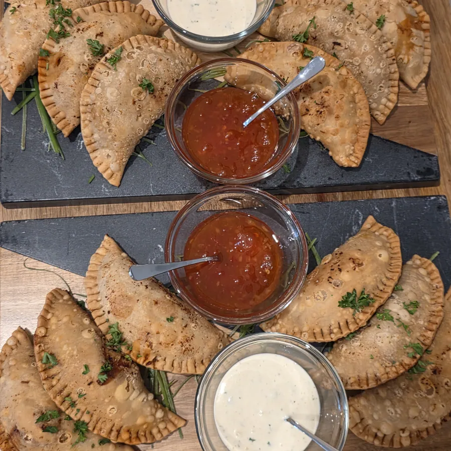 Overhead view of two slate boards of empanadas with red and white dipping sauces