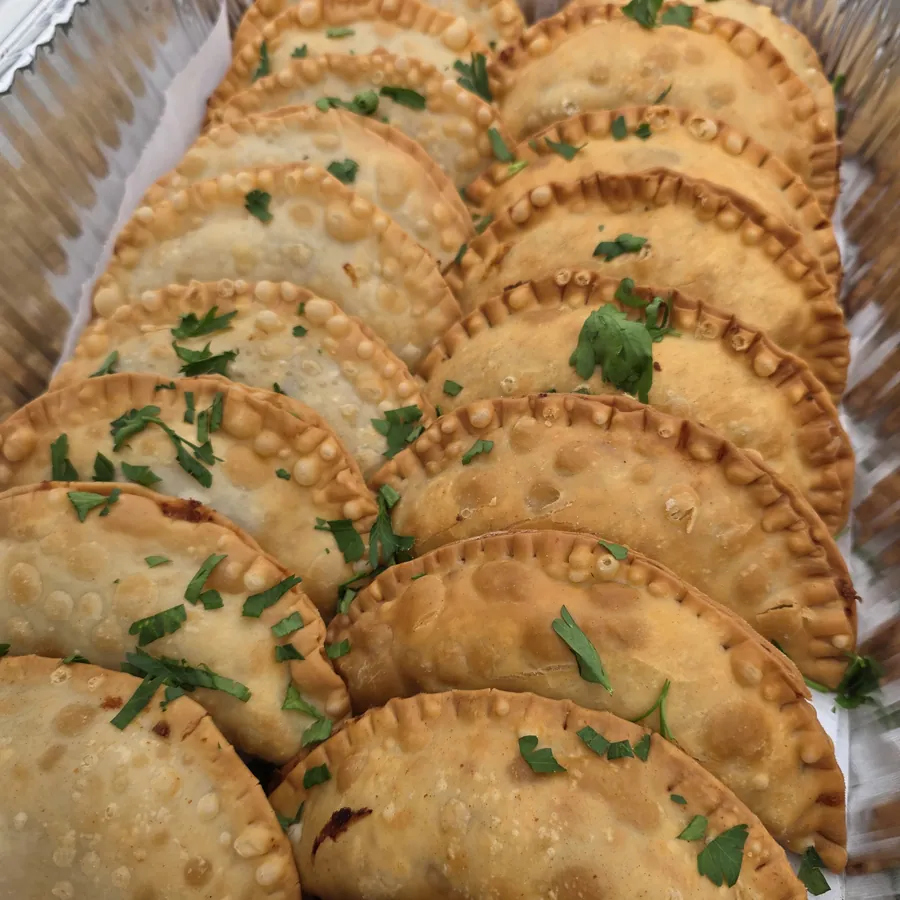 A full tray of golden empanadas topped with fresh parsley